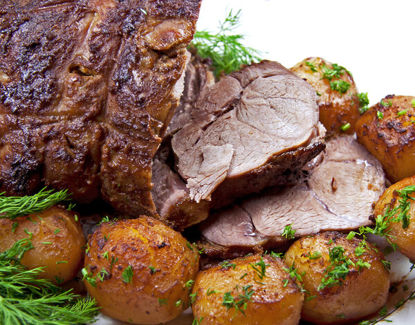 Closeup roast leg of lamb with potatoes and dill. Isolated over white.