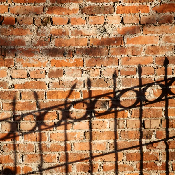Skuggan av ett staket på en tegelvägg — Stockfoto