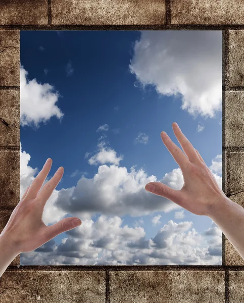 Две руки на окне со стеной и голубым небом — стоковое фото