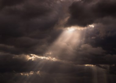 Sun ray trough black stormy cloudy sky clipart