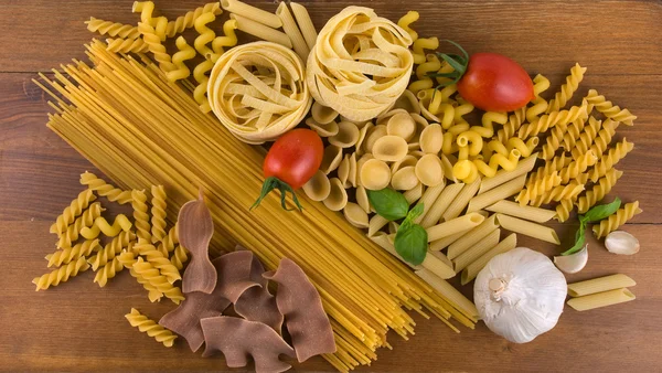 Different kind of raw pasta with tomatoes garlic and basil — Stock Photo, Image