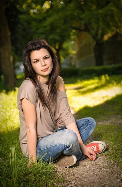 坐在美丽年轻黑发的肖像放宽在公园 — 图库照片
