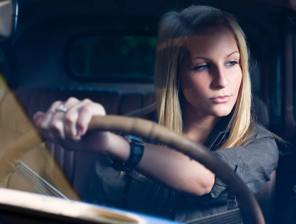Beautiful young blond girl in a black vintage car. — Stock Photo, Image