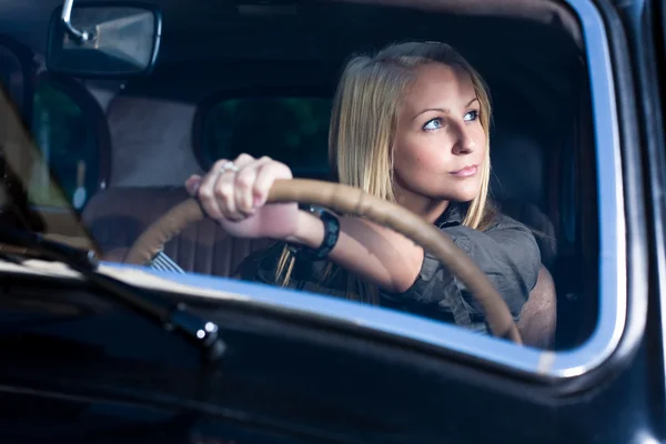 Beautiful young blond girl in a black vintage car. — Stock Photo, Image
