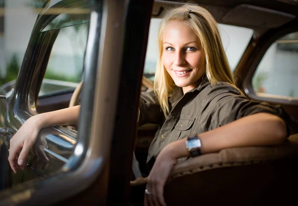 Vacker ung blond flicka i en svart vintage bil. — Stockfoto