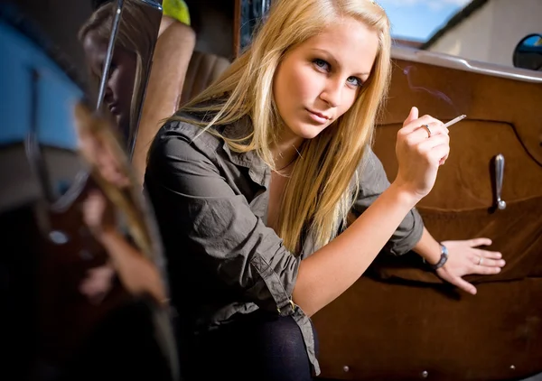 Beautiful young blond girl sitting in the door of a black vintag — Stock Photo, Image