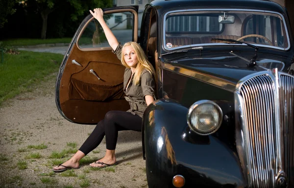 Beautiful young blond girl posing with a black vintage car — Stock Photo, Image