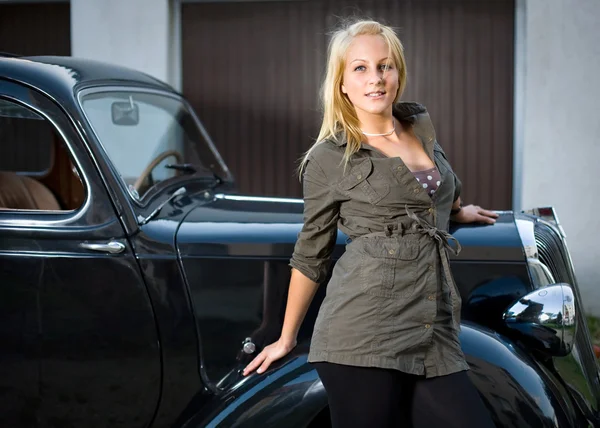 Beautiful young blond girl posing with a black vintage car. — Stock Photo, Image