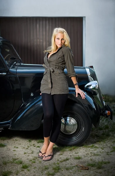 Szép fiatal szőke lány pózol egy fekete vintage autó. — Stock Fotó