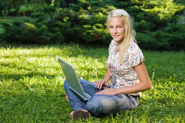 Hermosa rubia joven usando el ordenador portátil al aire libre en la naturaleza . — Foto de Stock