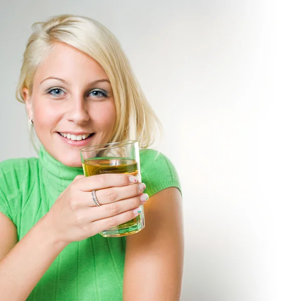 Beautiful young blonde girl holding a glass of apple juice, focu — Stock Photo, Image