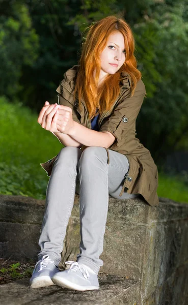 Romantic portrait of a young redhead girl sitting in the park. — Stock Photo, Image