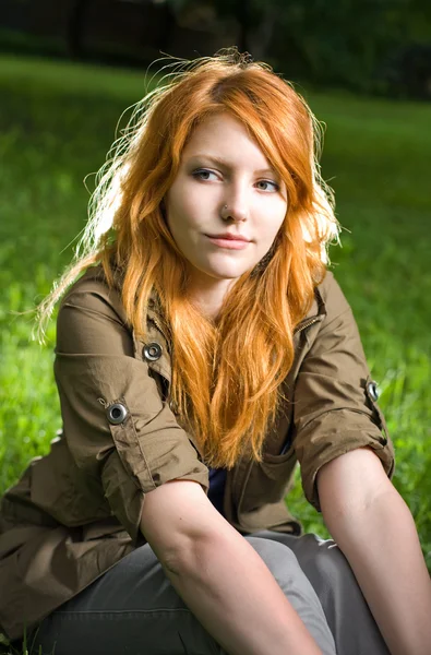 Romantisches Porträt eines jungen rothaarigen Mädchens, das im Park sitzt. — Stockfoto