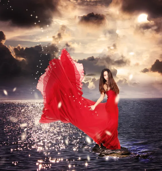 Κορίτσι στο κόκκινο φόρεμα στέκεται στους βράχους των ωκεανών — Φωτογραφία Αρχείου