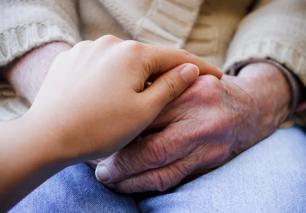 Jovem cuidador segurando as mãos do idoso — Fotografia de Stock