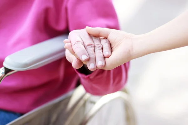 Старший леді в інвалідному візку, тримаючись за руки — стокове фото
