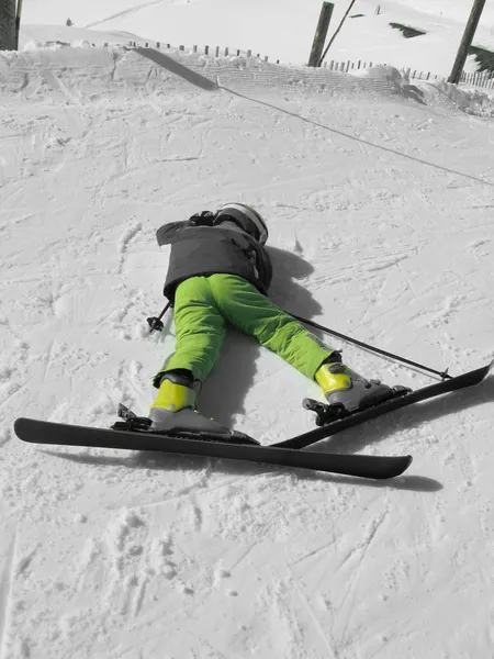 Child on skis and in a helmet lies on snow — Stok fotoğraf