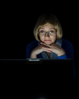 Mature woman working on laptop computer in night clipart