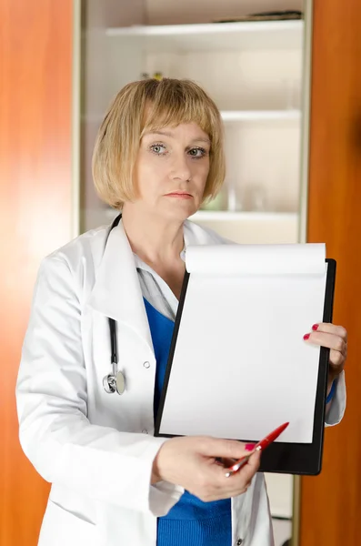 Mature woman doctor holding and showing blank clipboard — Stock Photo, Image