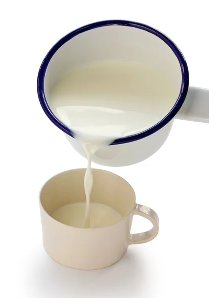 Pouring milk into a cup by an enamel milk pot — Stock Photo, Image