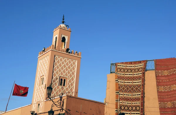 Tapis Marocains à vendre dans une boutique et minaret d'une mosquée à M — Photo