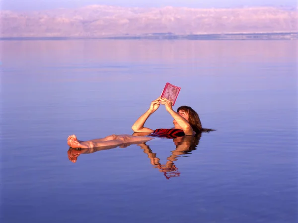 Дівчина, читаючи книгу в Мертвому морі Стокове Фото