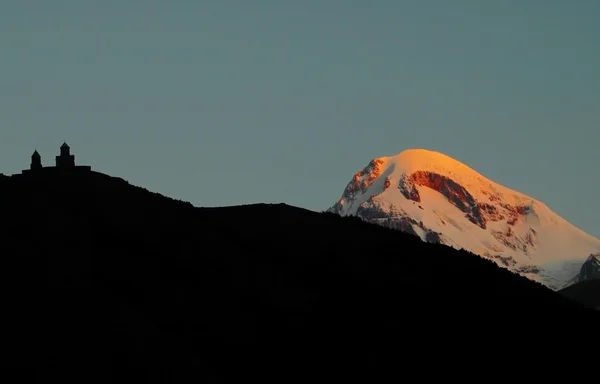 Sunrise kazbek Dağı üzerinde. sol tsminda sameba Manastırı silüeti — Stok fotoğraf