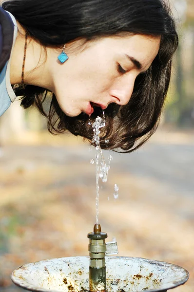 Uma jovem menina branca bonita bebe de uma fonte de bebida pública — Fotografia de Stock