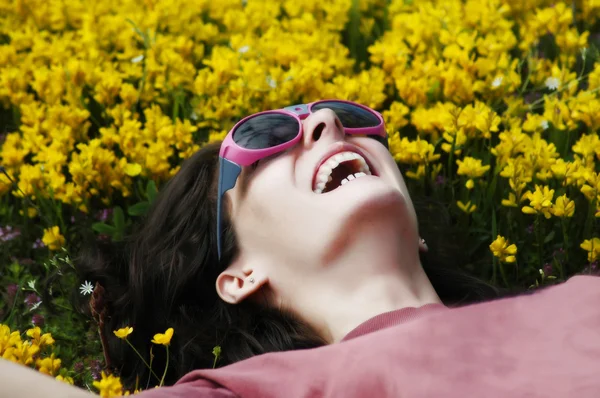 Beautiful young girl with sunglasses laying on yellow flowers — Stock Photo, Image