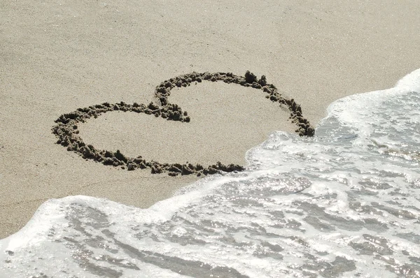 Handskrivna hjärtat på sand med vågen närmar sig — Stockfoto