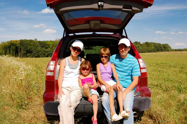 Lachende en gelukkige familie van vier in de buurt van hun auto op vakantiereis — Stockfoto
