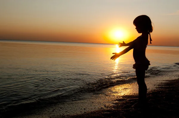 Детский силуэт на пляже на закате, маленькая девочка развлекается — стоковое фото