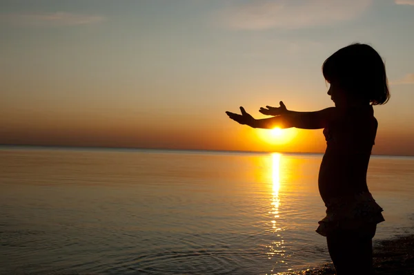 Silueta dítěte na pláži při západu slunce, holčička baví — Stock fotografie