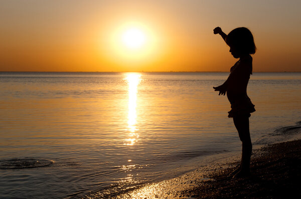 Child silhouette on sunset beach, little girl having fun
