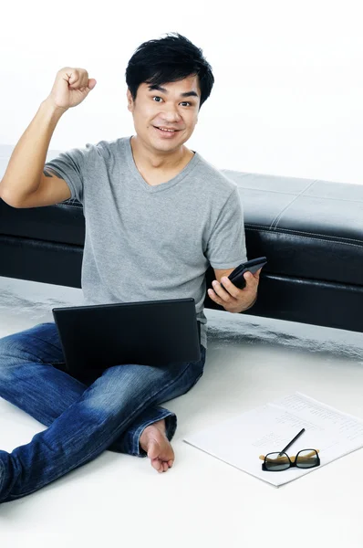 Excited young man sitting on floor with laptop — Stock Photo, Image