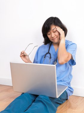 Overworked female doctor or nurse rubbing eyes at laptop compute clipart