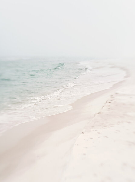 Soft atmospheric mood shot of beach and ocean on a misty, foggy day. Pastel tones, short depth of field. Focus on surf's edge.