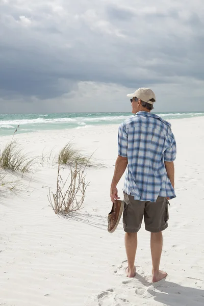 Érett férfi sétált a tengerparton, szállító cipő — Stock Fotó