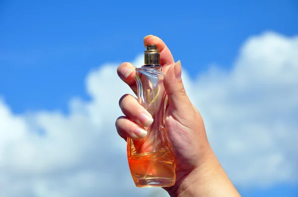 Bottle of perfume in the women\'s hand against the sky
