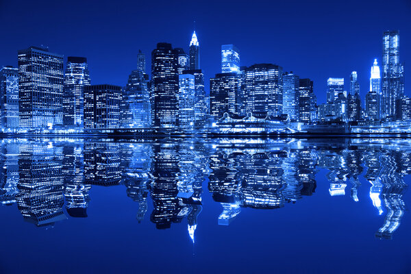 Lower Manhattan in New York City at night with reflection in water with blue hue