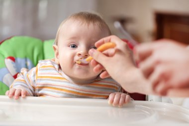 Mother feeding baby food to baby clipart