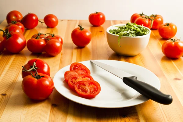 Skivad vinstockar tomater, ruccola och kniven på ett köksbord Stockbild