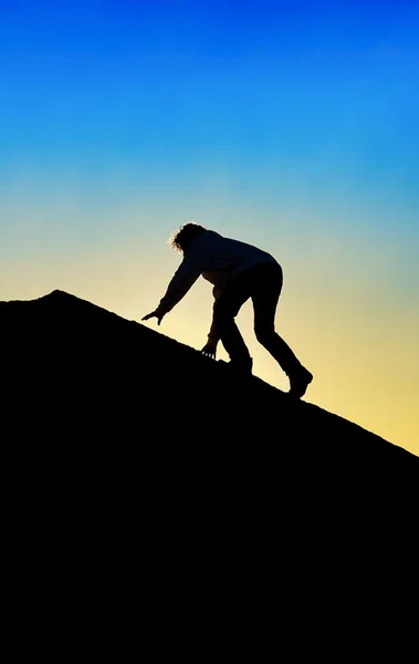 Silueta del hombre subiendo a la cima de una montaña — Foto de Stock