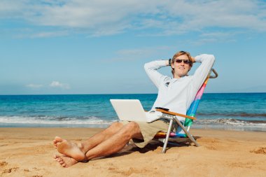 genç çekici adam dizüstü bilgisayar ile sahilde rahatlatıcı
