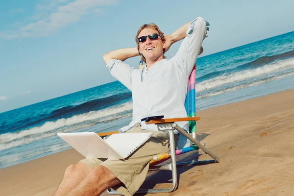 Hombre atractivo joven Relajarse en la playa con ordenador portátil — Foto de Stock