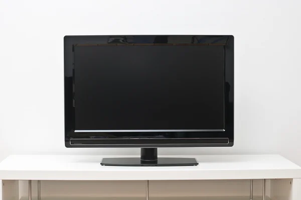 白色的表格和墙上的黑色纯平电视机 — 图库照片