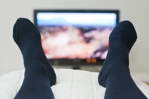 Acostado en la cama y viendo la televisión en calcetines oscuros — Foto de Stock