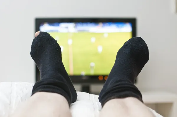 Deitado na cama e assistindo a um jogo na TV em meias escuras com um buraco — Fotografia de Stock