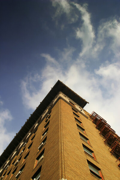 Photo of brick building from below with blue sky and white clouds creating a vortex