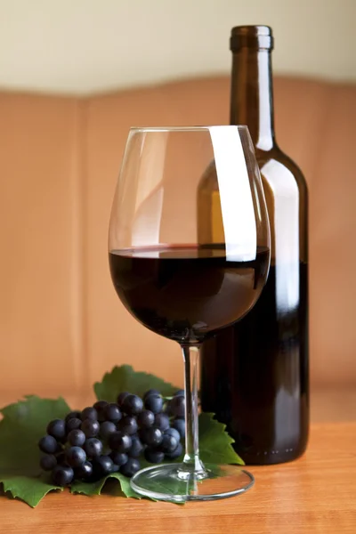 Un vin de sticlă cu o sticlă de vin roșu pe masă — Fotografie, imagine de stoc